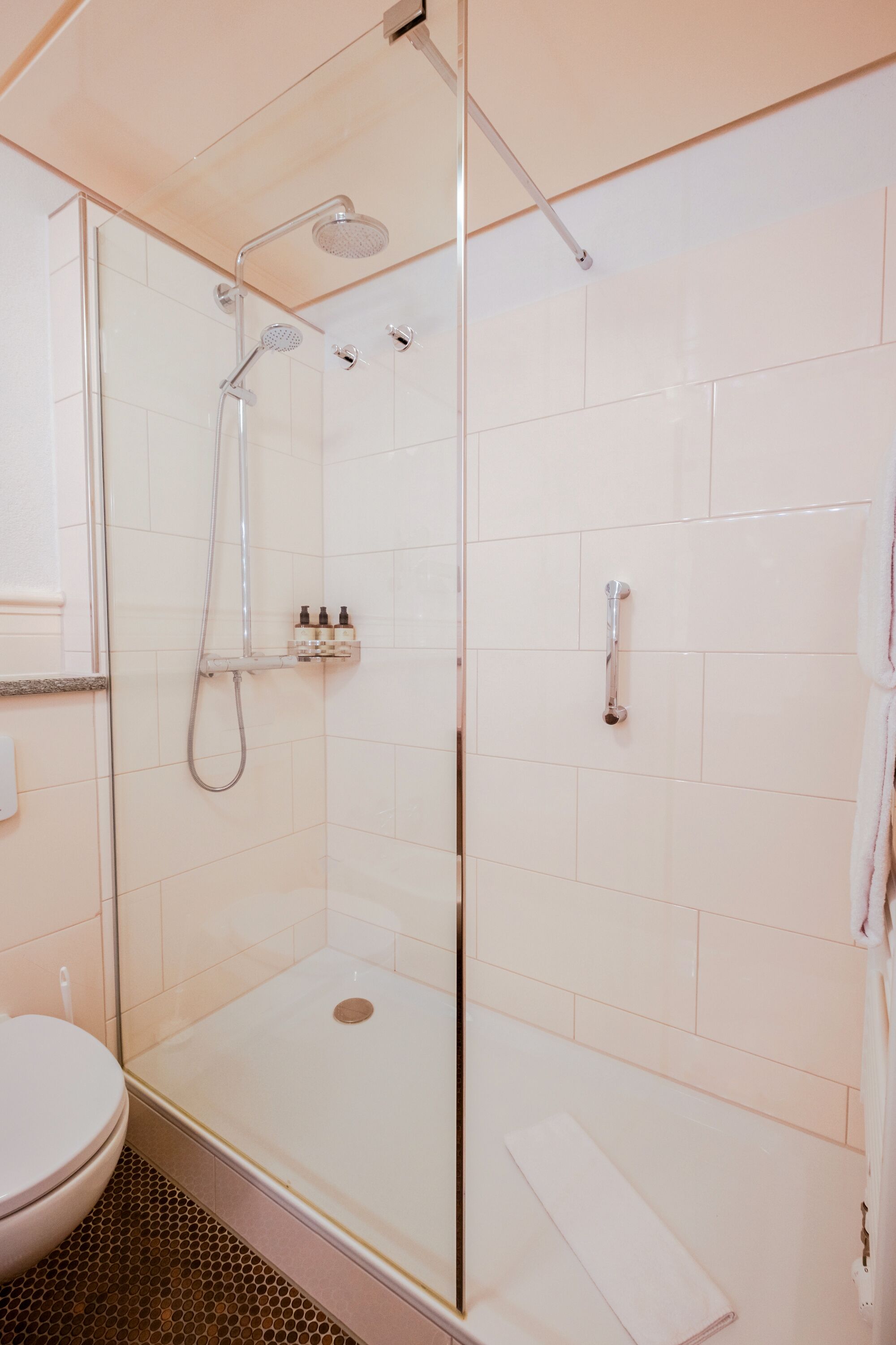 A glass-enclosed shower stall with a handheld showerhead, a handheld showerhead, and a wall-mounted faucet.