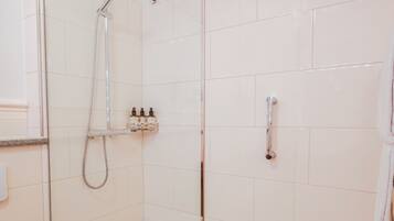 A glass-enclosed shower stall with a handheld showerhead, a handheld showerhead, and a wall-mounted faucet.