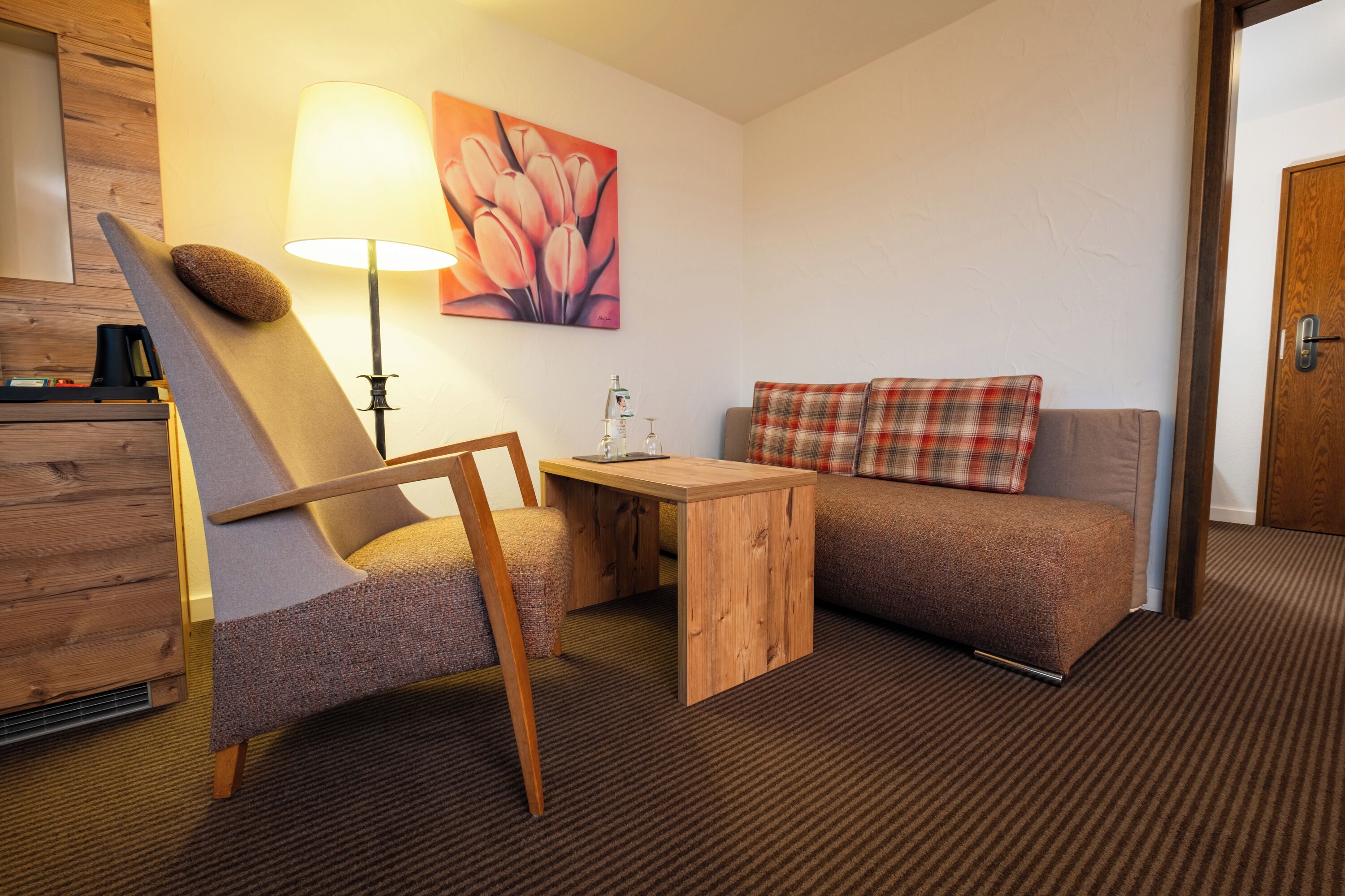 Une pièce comprenant une chaise en bois, une petite table, un canapé, une lampe et un tableau accroché au mur.