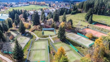 Eine Vogelperspektive auf einen Sportkomplex mit mehreren Tennisplätzen, umgeben von Bäumen und Gebäuden.