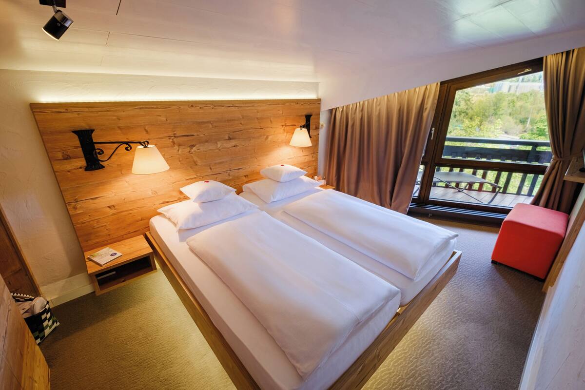 A double bed with two bedside tables, a window with curtains, and a view of the outdoors.