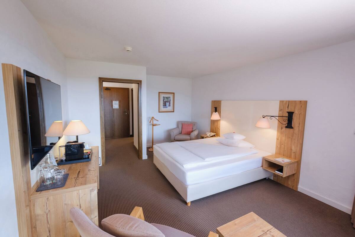 A hotel room with a bed, bedside tables, a desk, a chair, and a television.