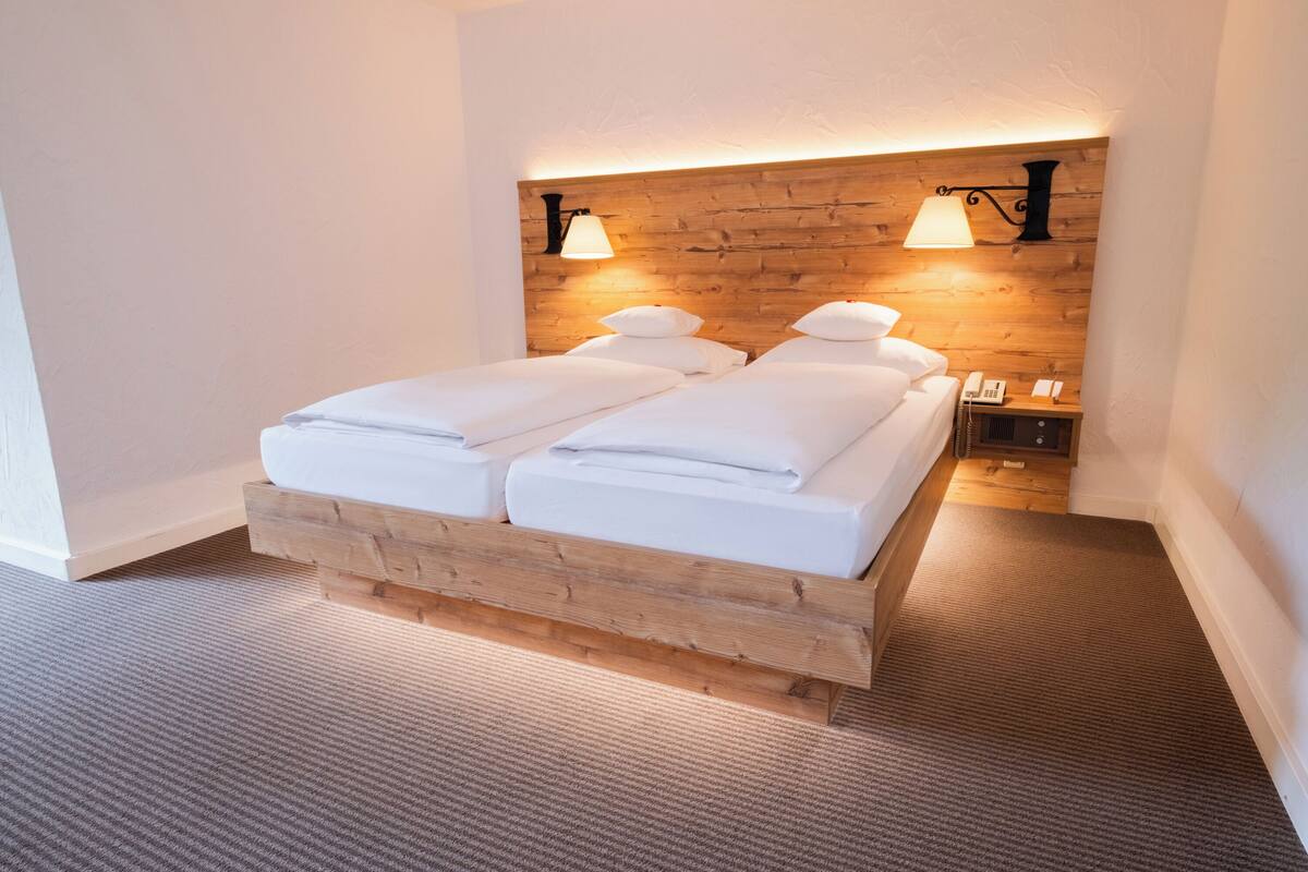 A double bed with a wooden headboard, two bedside lamps, a bedside telephone, and a small bedside table.