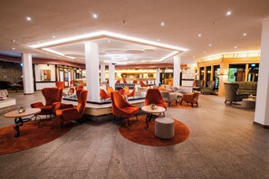 A spacious lobby with modern orange chairs, a central round table, and a stone accent wall. - Vier Jahreszeiten am Schluchsee (Schluchsee)