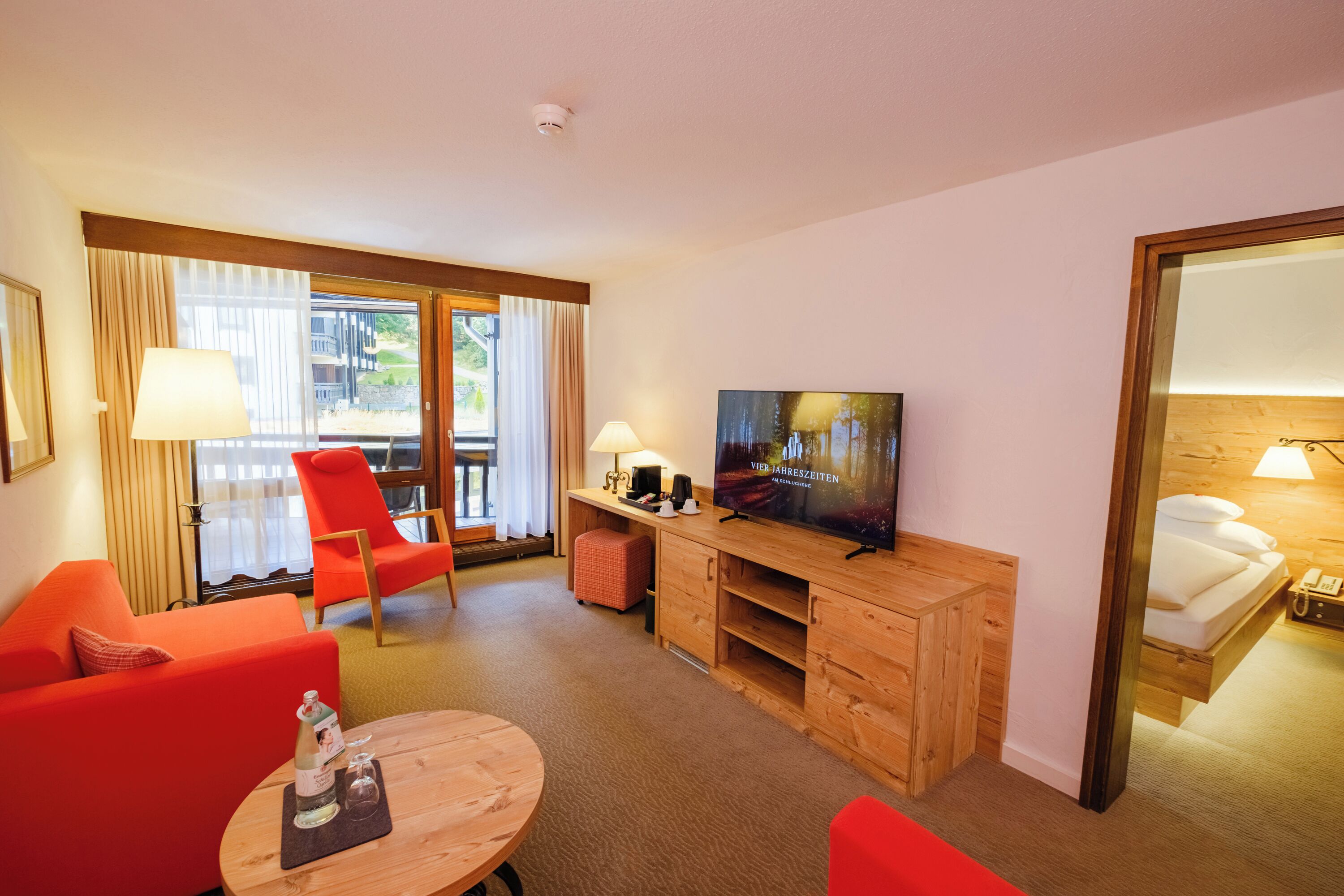 Une chambre d’hôtel avec une télévision, des fauteuils rouges, un bureau en bois et un lit.