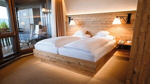 A double bed with a wooden headboard, a bedside table with a lamp, and a view through a window.