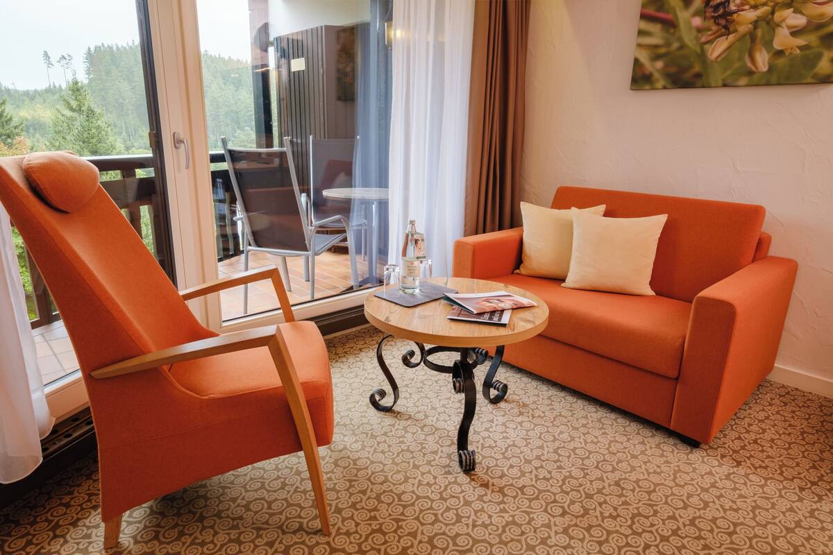 A room with a sofa, armchair, and a small table with a glass.