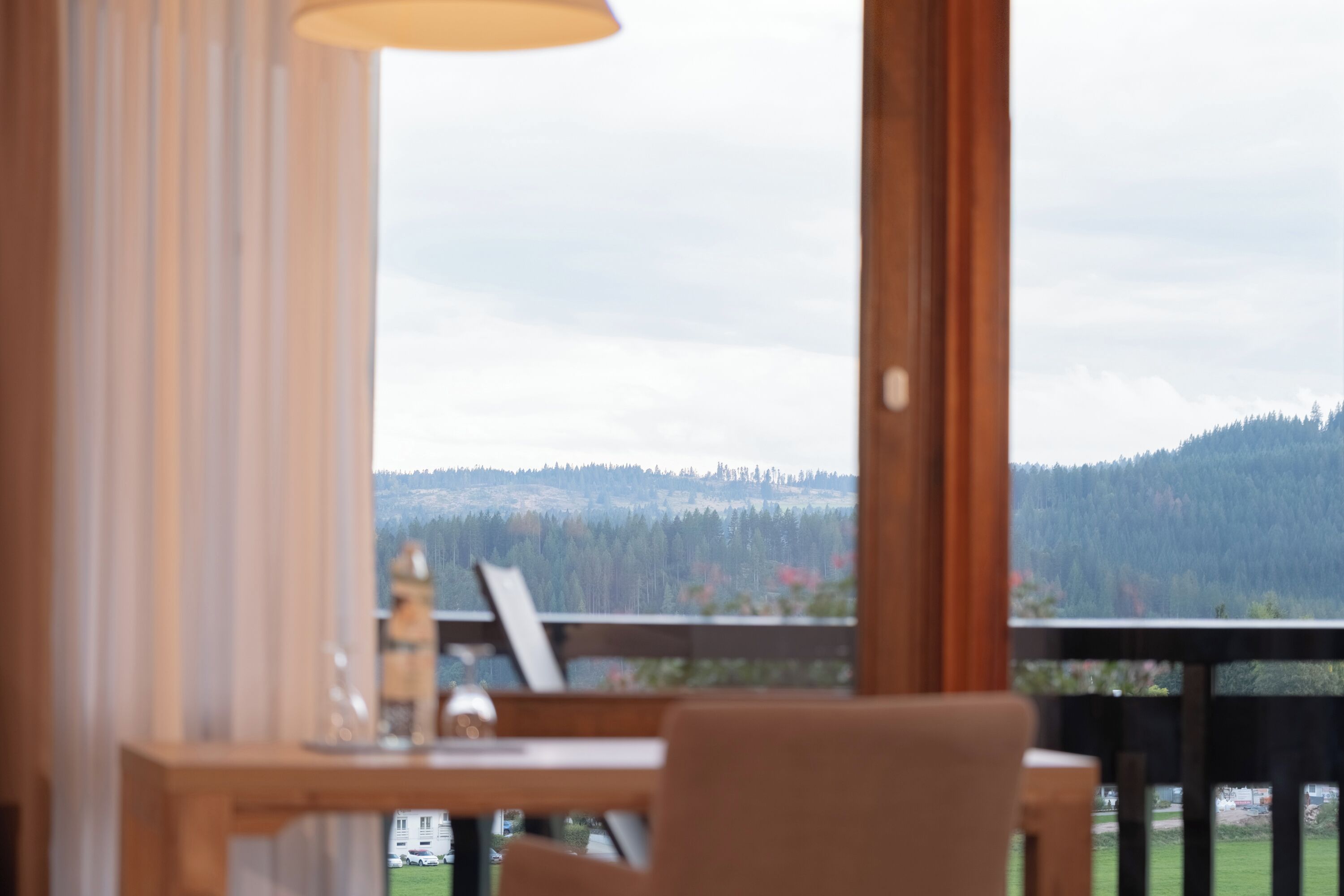 A room with a view of a forested mountain range, a wooden desk, and a lamp.