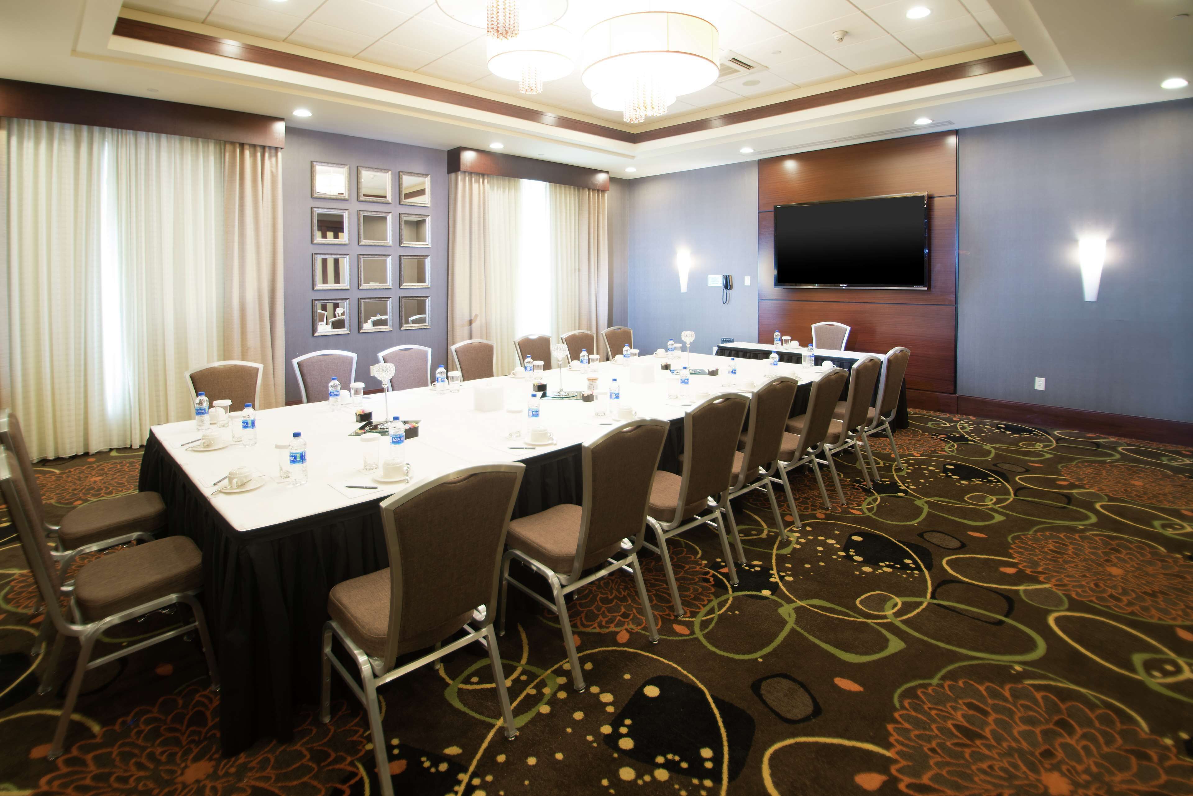 A conference room with a long table, chairs, a flat-screen TV, and a carpeted floor.