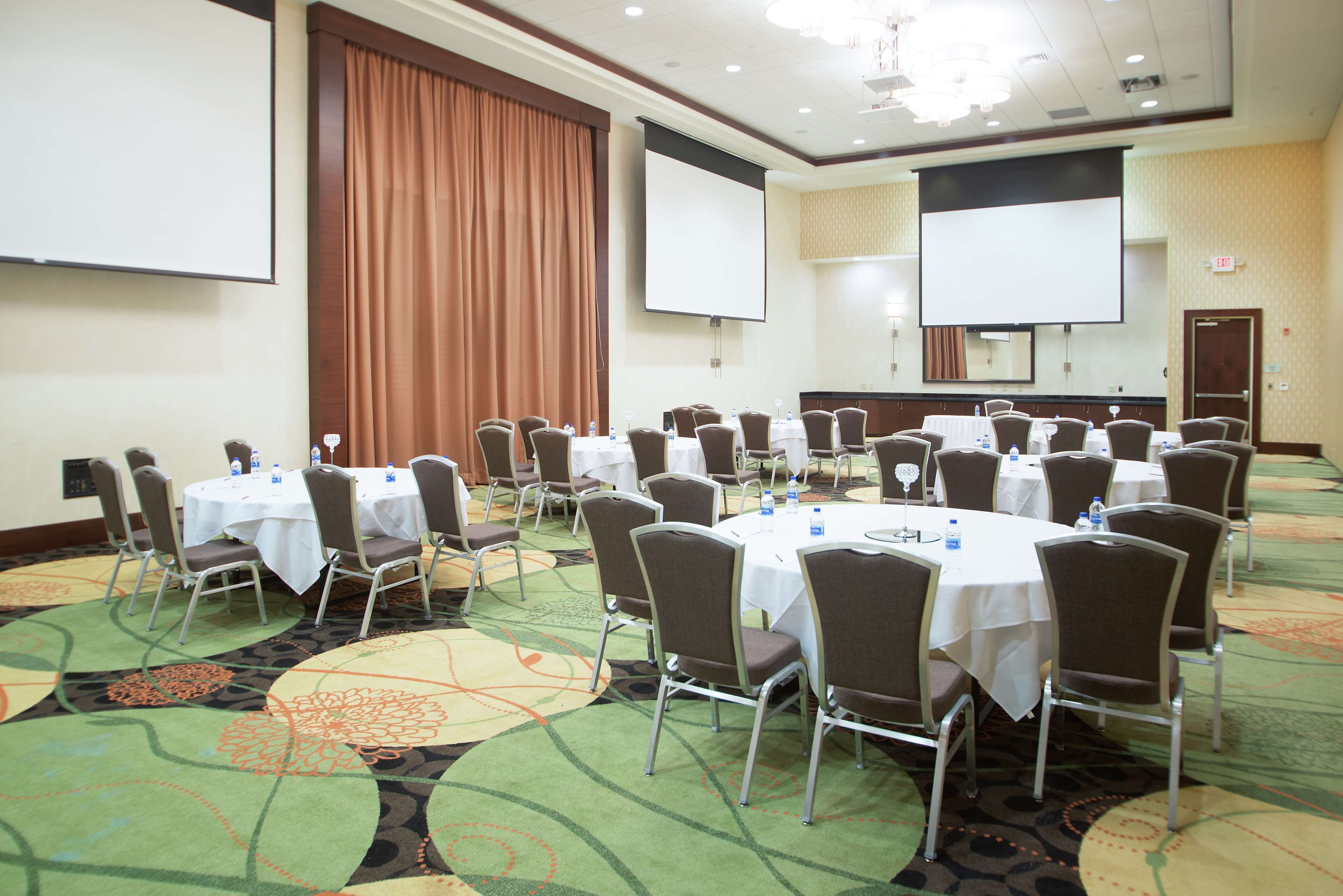 Une salle de conférence équipée de tables rondes, de chaises et d’écrans de projection.