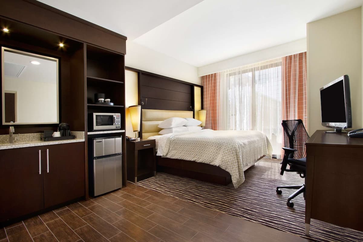 A hotel room with a bed, a desk, a chair, a TV, a microwave, a refrigerator, and a bathroom.