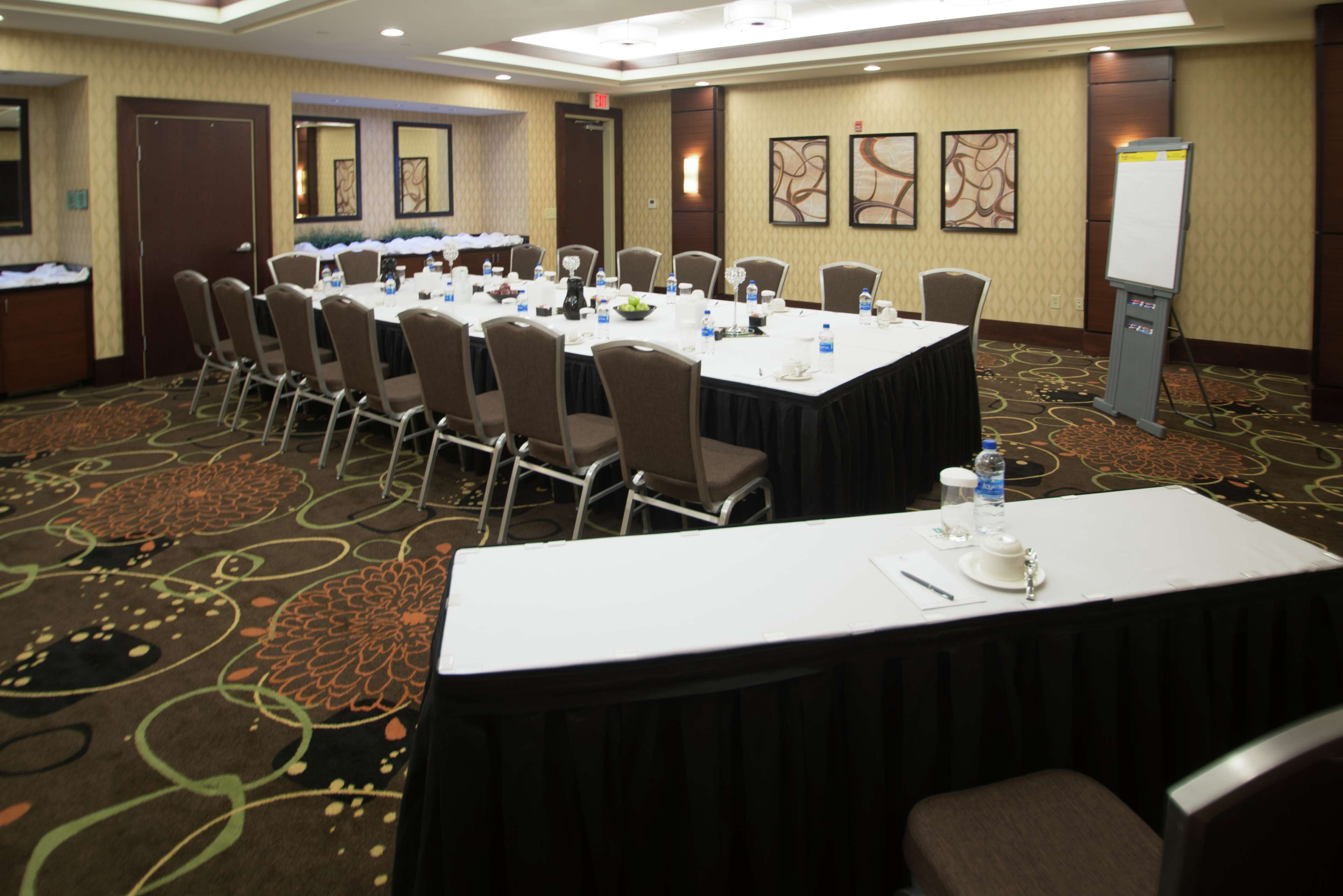 Une salle de conférence avec une longue table, de nombreuses chaises, des bouteilles d’eau et un présentoir pour tableau blanc.