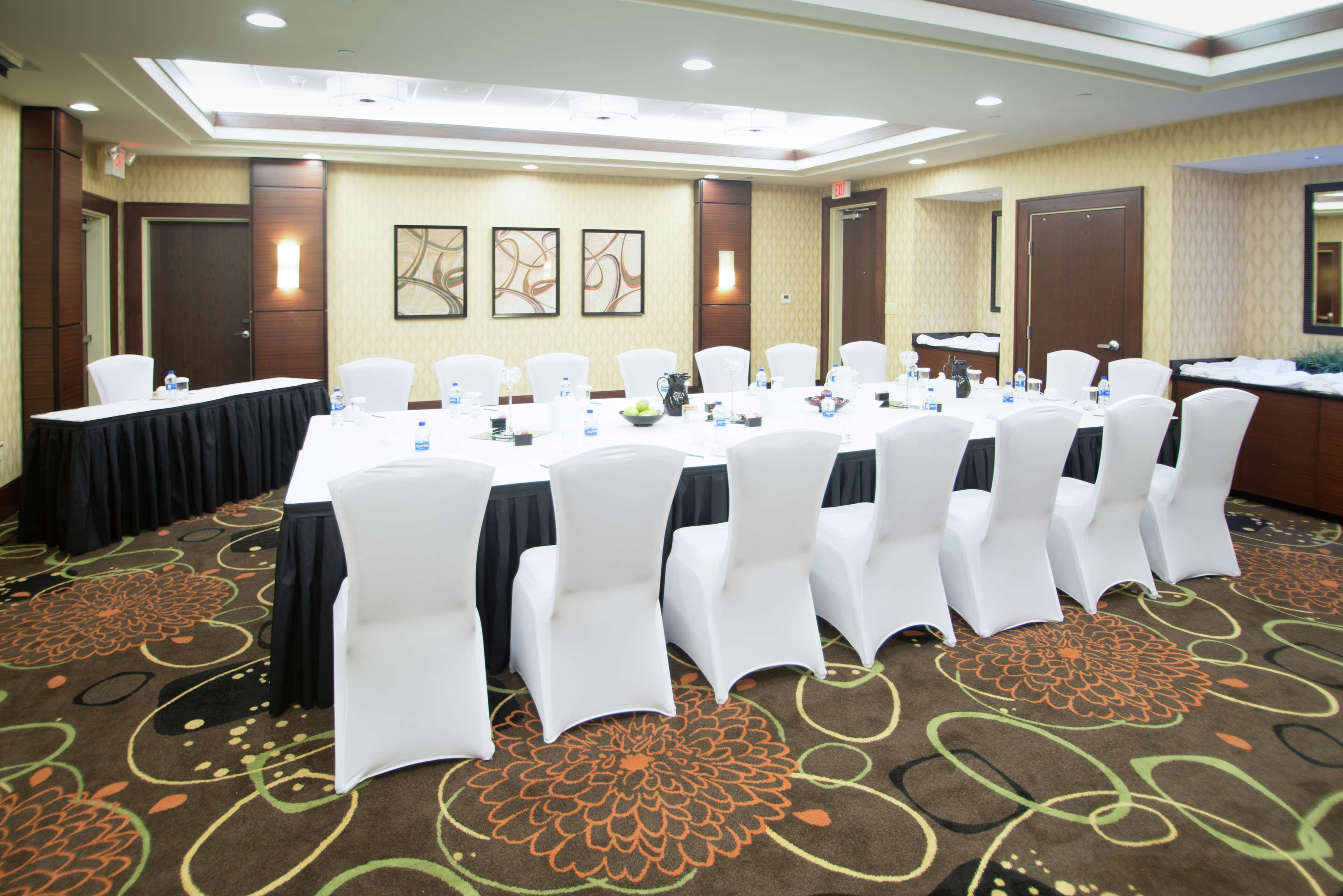 A conference room with a long table, white chairs, and a carpeted floor.