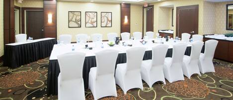 A conference room with a long table, white chairs, and a carpeted floor.