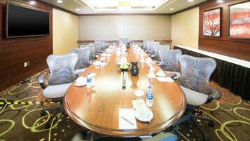A conference room with a long table, chairs, a TV, and a carpeted floor.