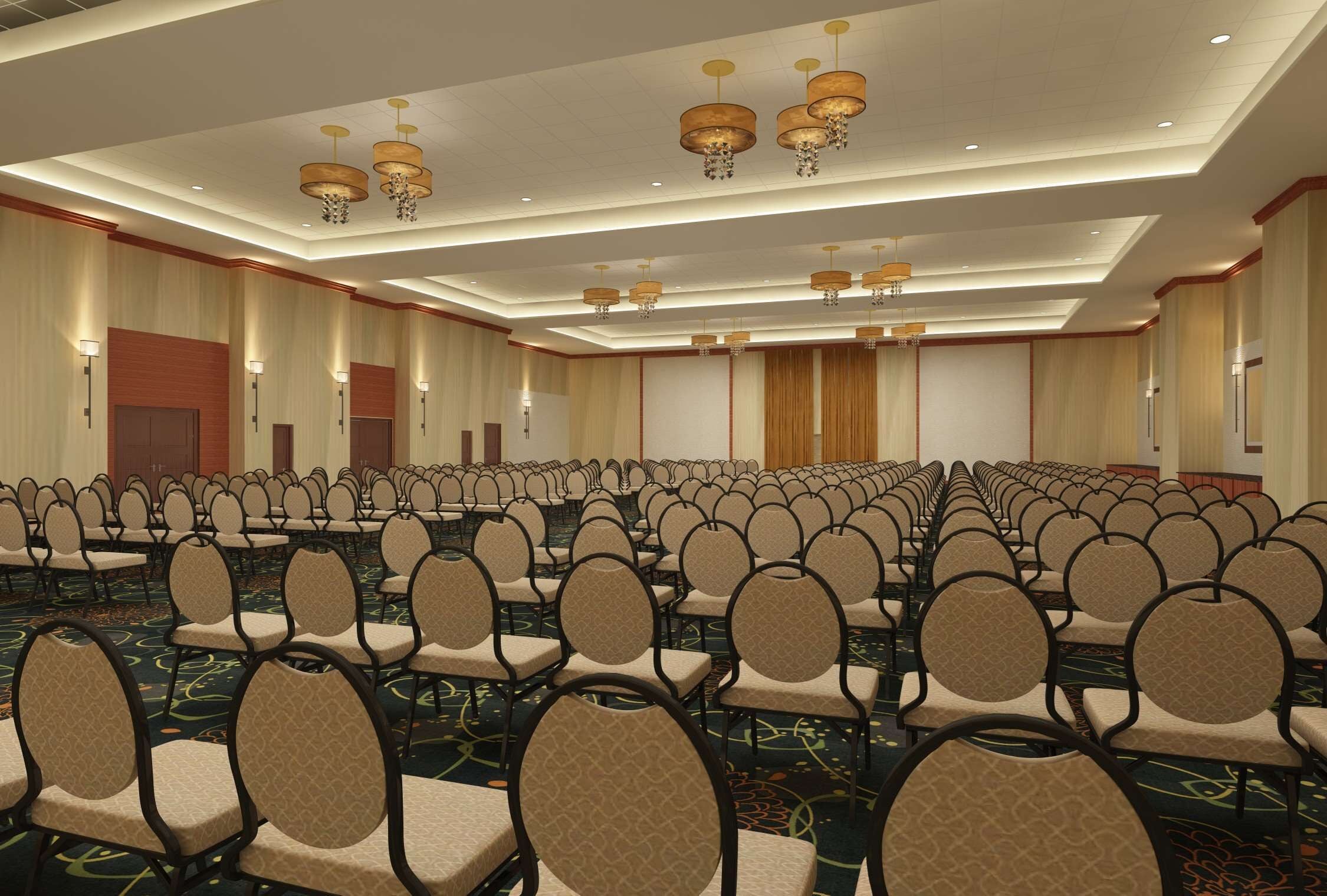 A large conference room with rows of chairs, a patterned carpet, and chandeliers.
