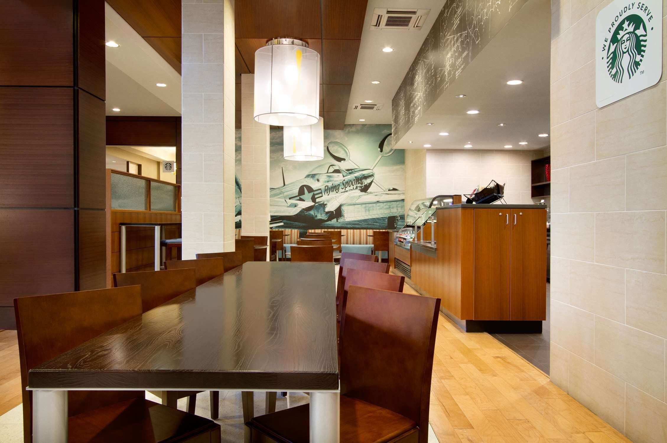 A spacious restaurant with wooden tables and chairs, a large mural of a vintage airplane, and a Starbucks logo on the wall.