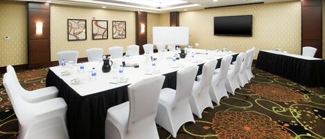 A conference room with a long table, white chairs, and a flat-screen TV on the wall.