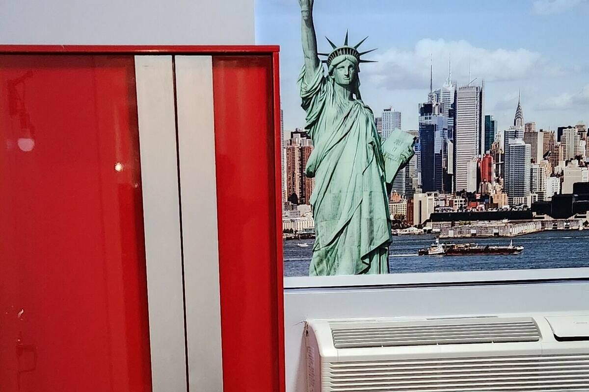 Une chambre à coucher avec un lit, une armoire rouge et une fresque représentant la Statue de la Liberté.