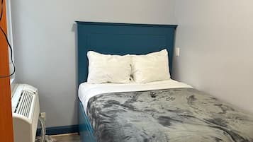 A single bed with a teal headboard, white bedding, and a gray patterned blanket.
