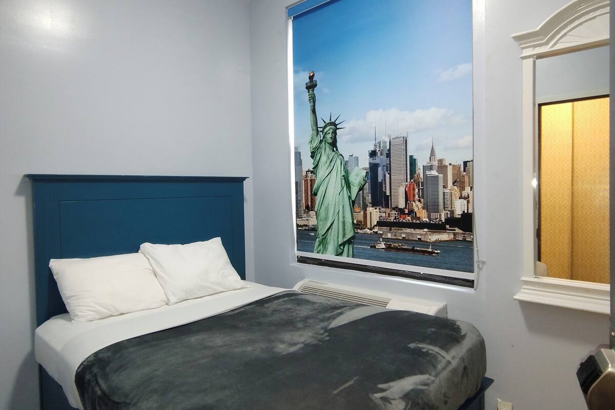 Une chambre à coucher avec un lit, une fenêtre ornée d’une fresque représentant un paysage urbain et une tête de lit bleue.