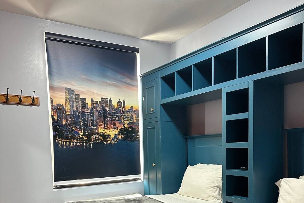 Une chambre avec deux lits, une affiche représentant un paysage urbain accrochée au mur et une armoire bleue.