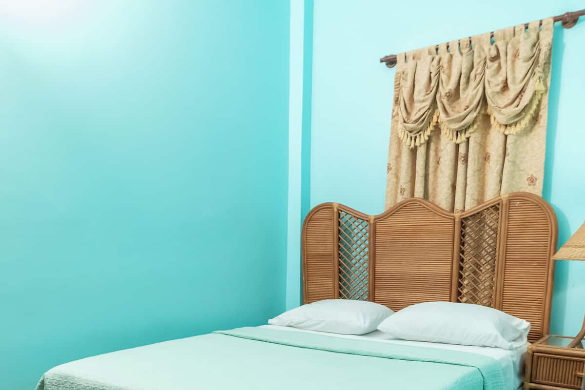 A room with a bed, a wooden headboard, a nightstand, and a window with curtains.