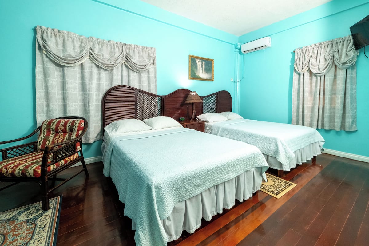 A room with two beds, a chair, and a painting on the wall.