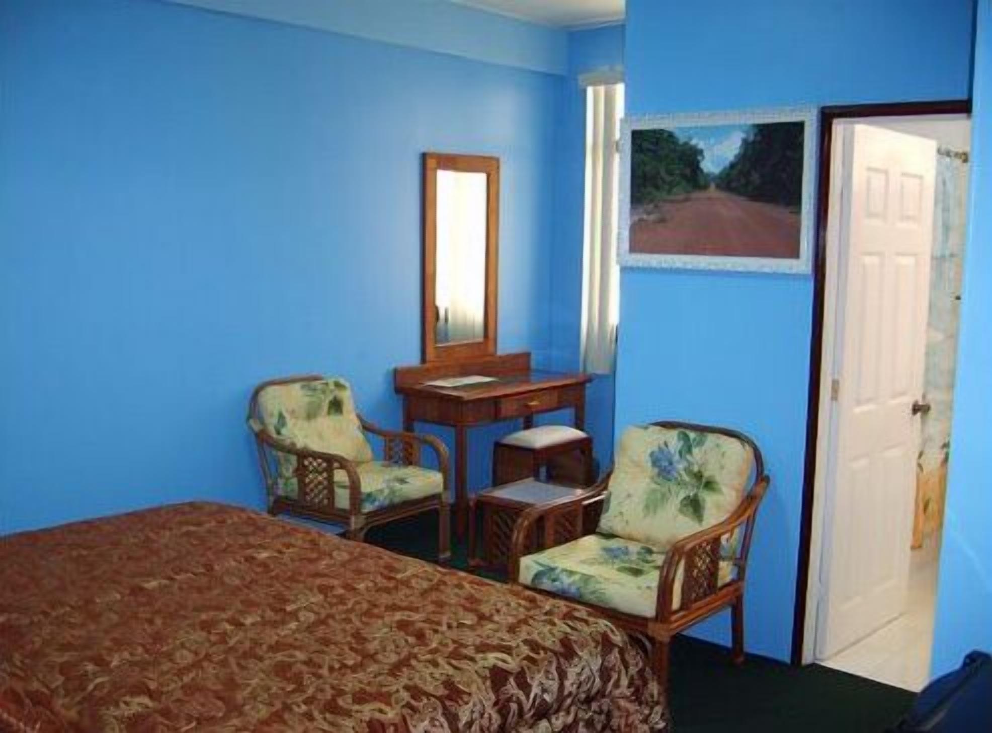 A room with a bed, two chairs, a desk, and a door.
