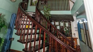 Un escalier en bois à plusieurs niveaux, doté de rampes, une zone recouverte d’une moquette bleue et un climatiseur fixé au mur.