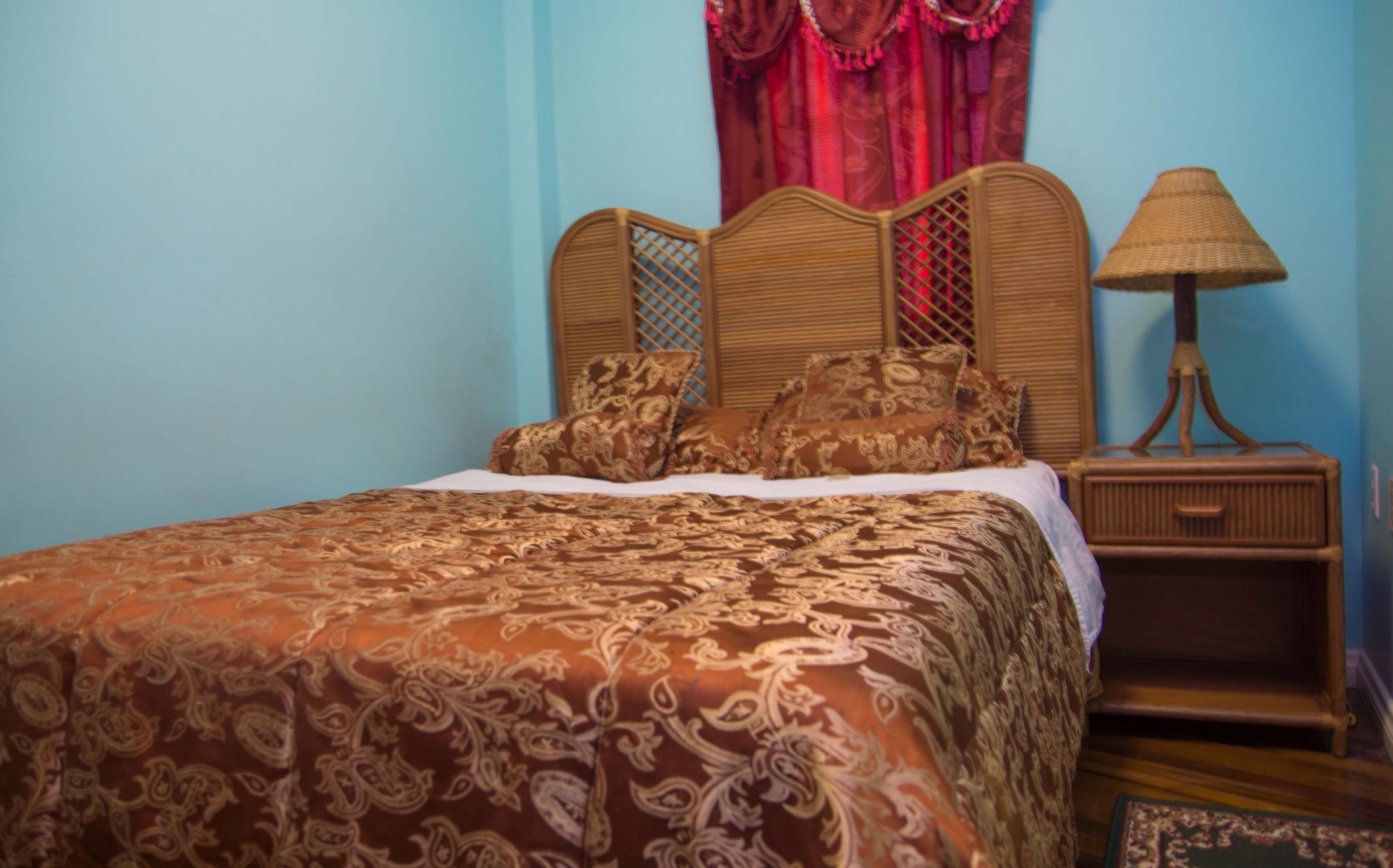 A bed with a patterned bedspread, a wooden headboard, and a nightstand with a lamp.
