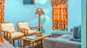 Ein Wohnzimmer mit zwei Korbstühlen, einem kleinen Tisch mit Lampe und einem Sofa.
