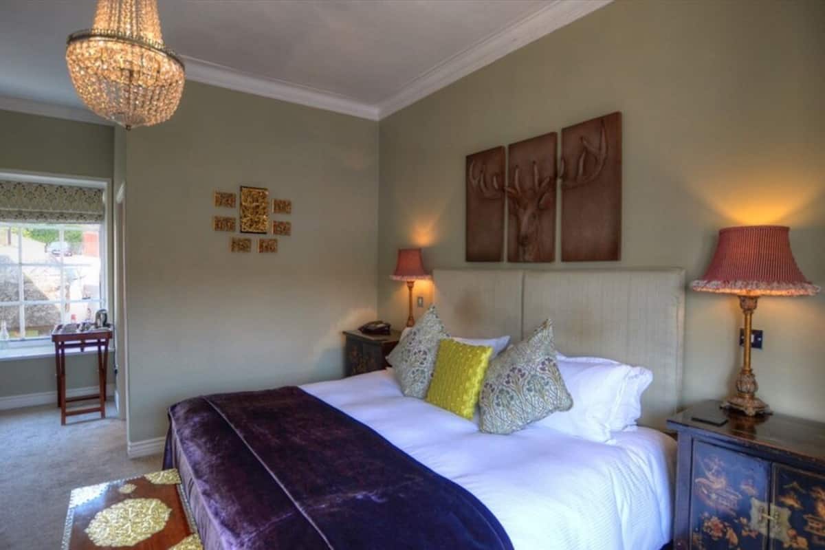 A bedroom with a large bed, two bedside tables, a chandelier, and wall art.