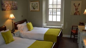 A hotel room with two beds, a desk, a chair, and a window.