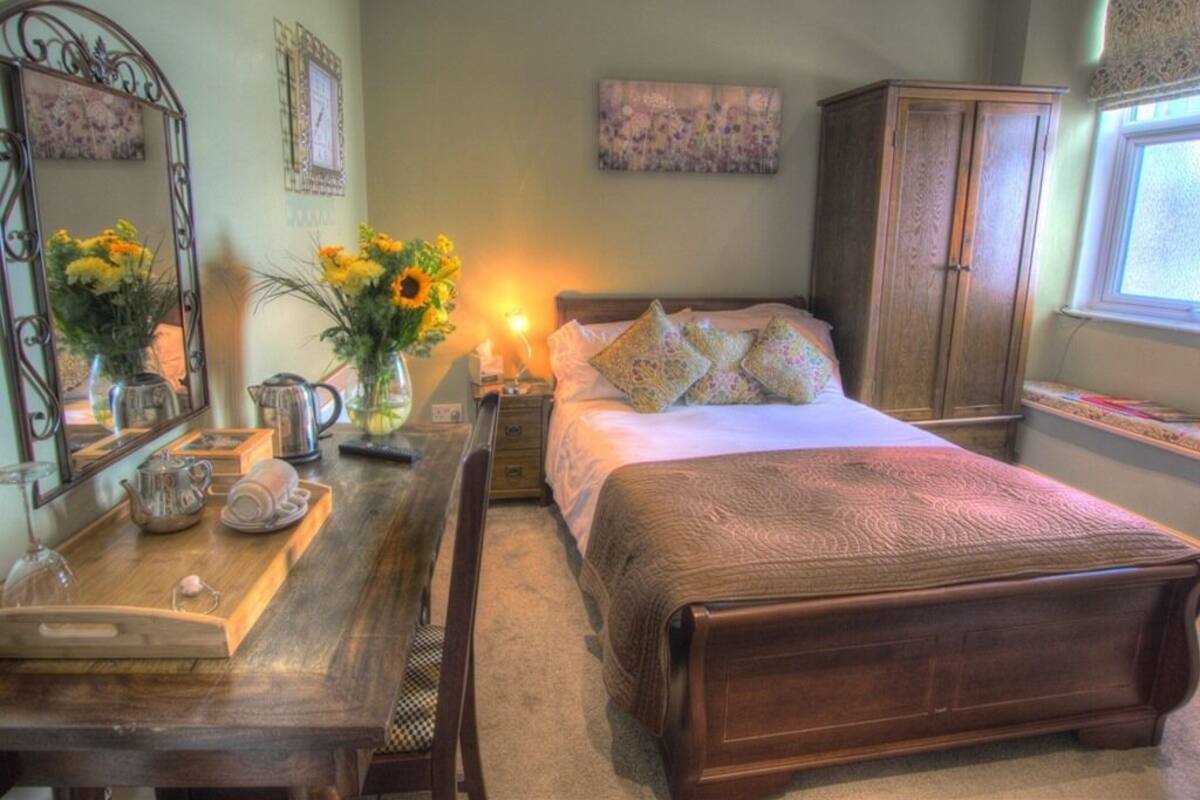 A bedroom with a wooden bed, a nightstand, a dresser, and a desk with a vase of flowers.