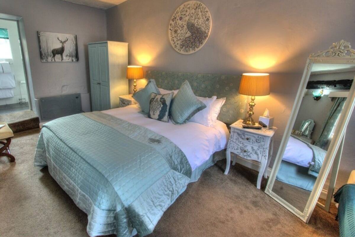 A bedroom with a bed, two bedside lamps, a mirror, a dresser, and a wall with a deer painting.