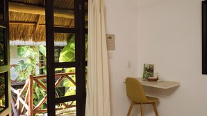 A room with a wooden desk, a chair, a patterned rug, a thatched roof outside, and a sliding glass door. - Kin Ha Tulum Hotel (Tulum)