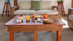 A wooden table with breakfast items, a wicker sofa with cushions, and a thatched roof structure. - Kin Ha Tulum Hotel (Tulum)
