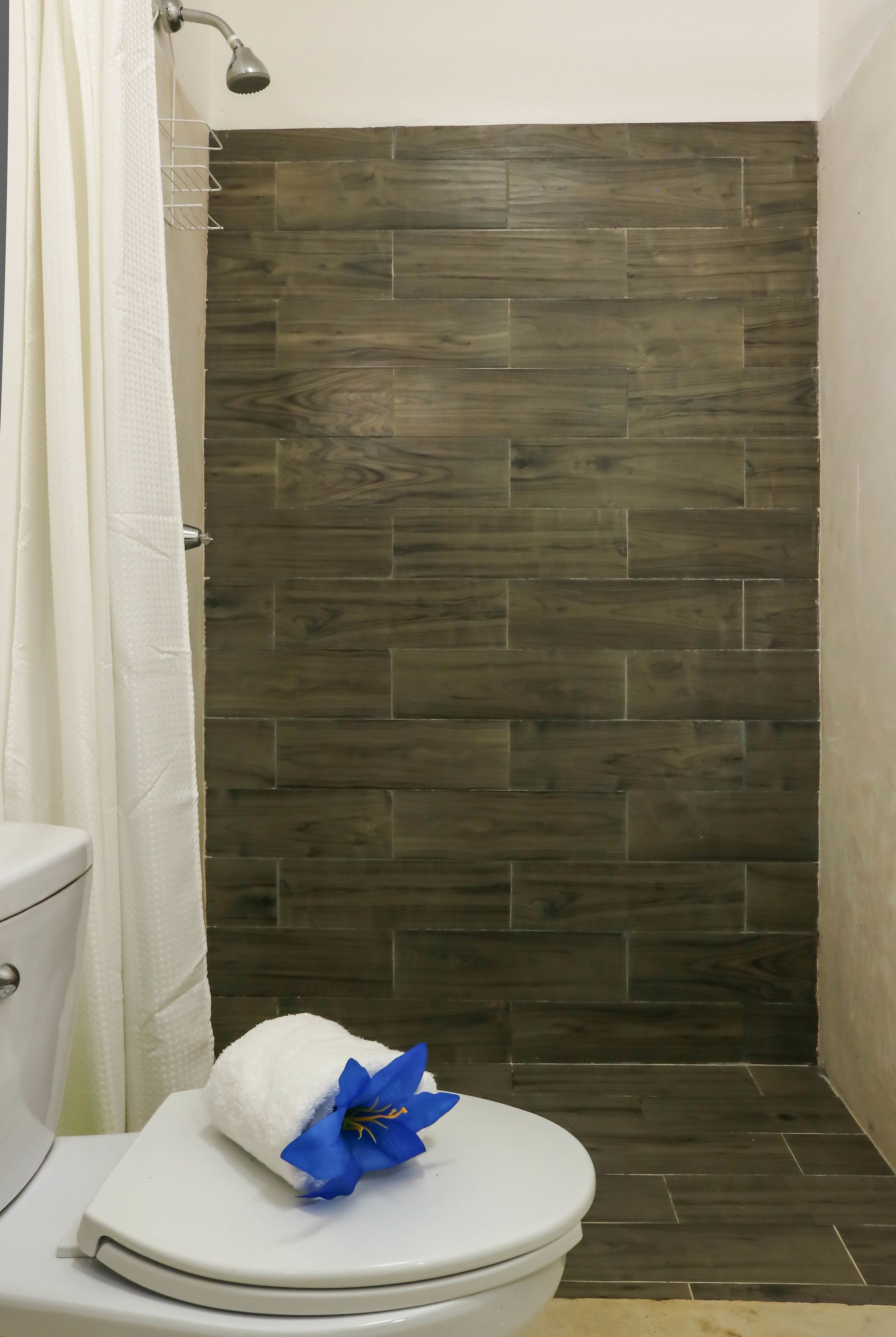 Un bagno con il water, una doccia con parete in legno scuro e un asciugamano con un fiore blu sul coperchio del water.