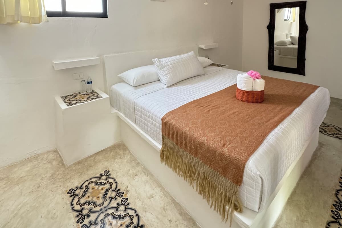 A bedroom with a bed, a ceiling fan, a window with curtains, a nightstand, and a patterned rug.
