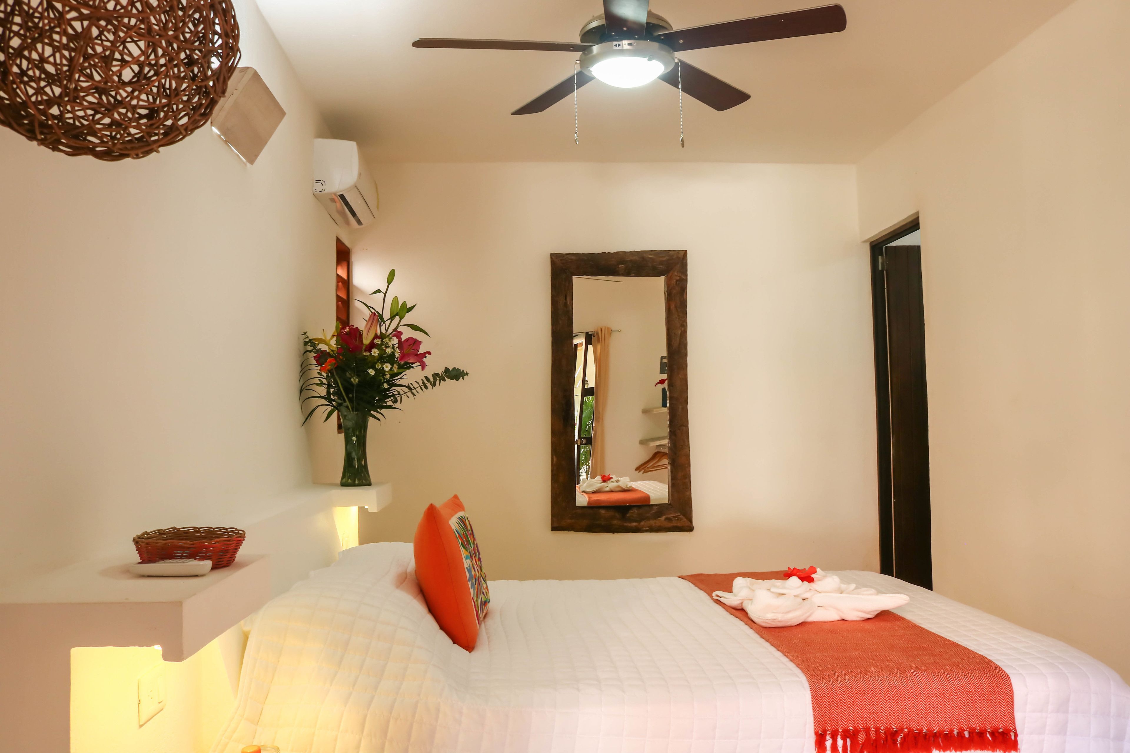 A hotel room with a bed, a ceiling fan, a mirror, and a wall-mounted air conditioner.