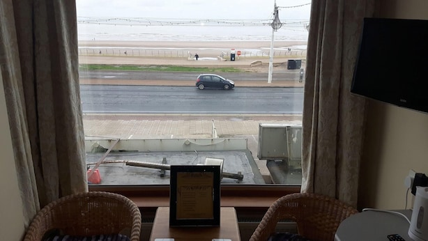 A room with a view of the beach, a table with a framed certificate, and two wicker chairs. - The Fame (Blackpool)