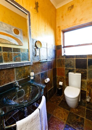 Une salle de bain avec un lavabo en verre, des toilettes et un miroir.
