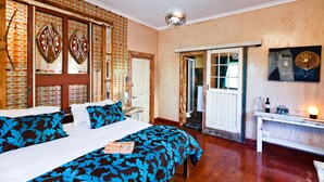 A hotel room with a large bed, a desk with a lamp, and a door leading to a bathroom. - Sweet Olive Guesthouse (Cape Town)