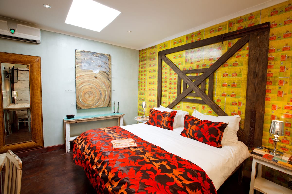 Habitación de hotel con una cama grande, cabecero de madera, un cuadro en la pared y una ventana con marco de madera.