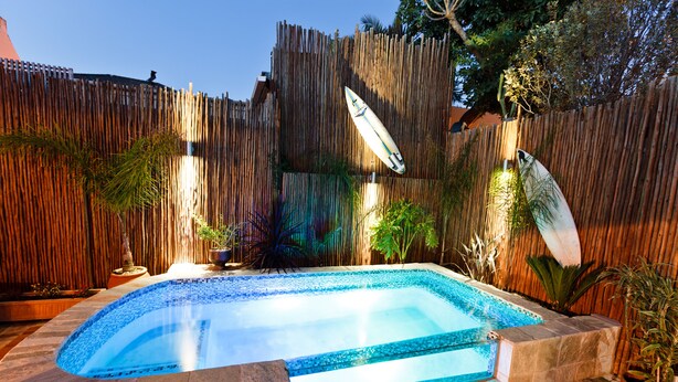 A rectangular swimming pool with a tiled edge, surrounded by a wooden fence and potted plants. - Sweet Olive Guesthouse (Cape Town)