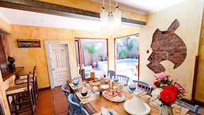 A dining area with a wooden table set for a meal, chairs, and a decorative wall piece. - Sweet Olive Guesthouse (Cape Town)