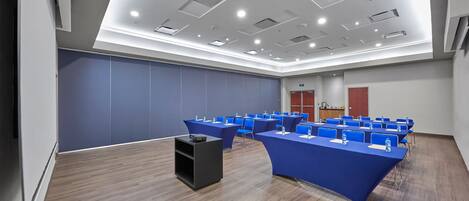 Un salón de conferencias con varias mesas y sillas, un atril y un ventanal grande.