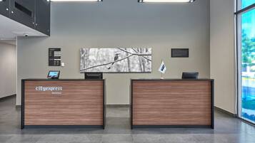 Una recepción con la marca 'cityexpress hotels', una pantalla digital y una obra de arte enmarcada en la pared.