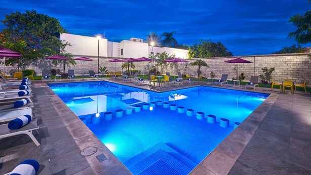 A swimming pool with lounge chairs and umbrellas, surrounded by a stone wall and trees.